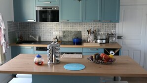 Una cocina con gabinetes color turquesa, una isla de madera, taburetes blancos y una araña.