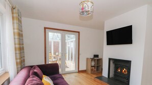 A living room with a purple sofa, a fireplace, a television, and a sliding glass door leading to an outdoor area. - Doire An Daimh (Acharacle)
