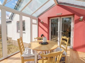 Une véranda avec une table et des chaises en bois rondes, un vase et un mur rouge.