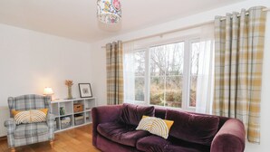 A living room with a purple sofa, a plaid armchair, and a white shelving unit. - Doire An Daimh (Acharacle)