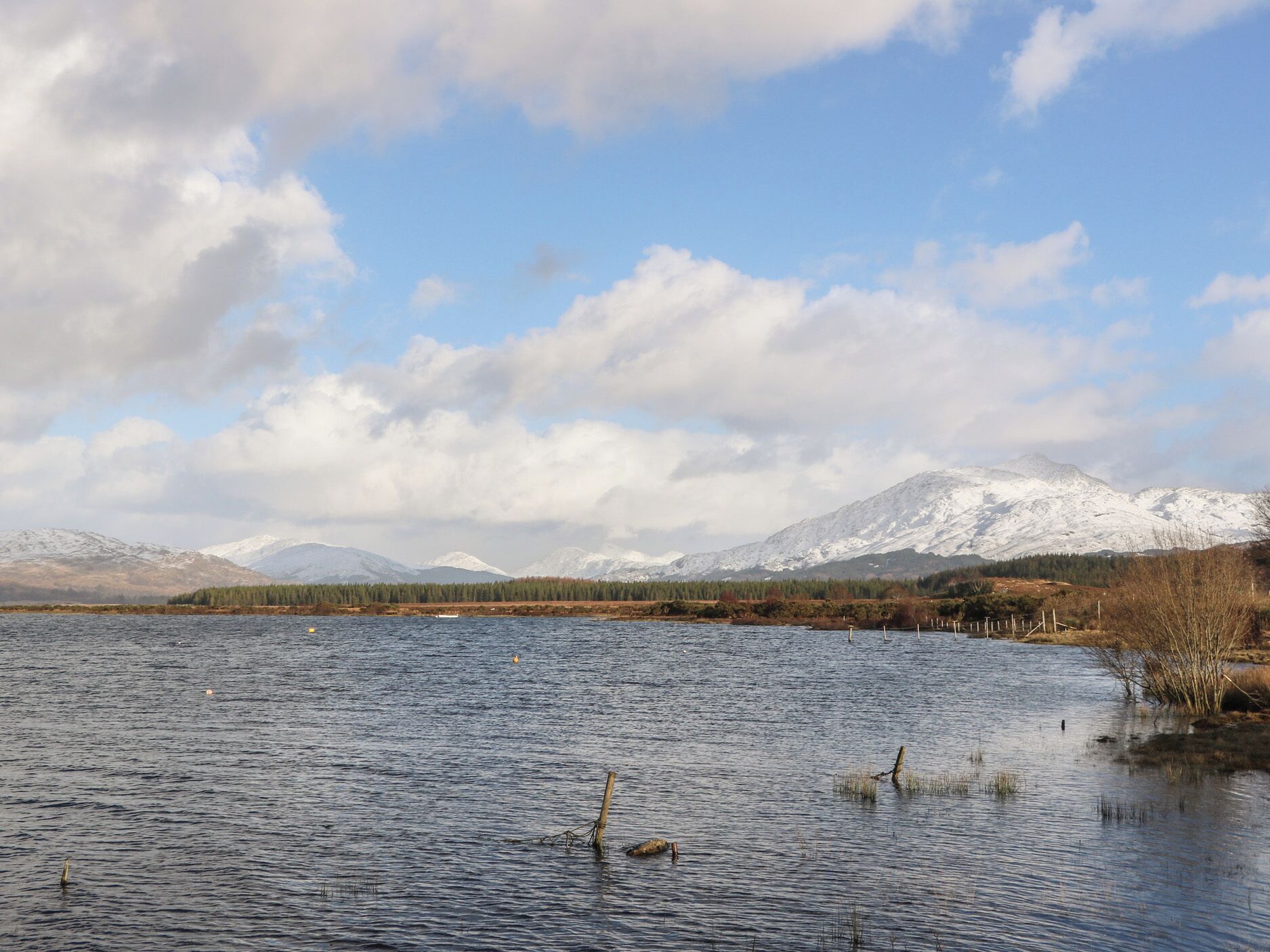 A calm lake with snow-capped mountains in the background and a clear sky.