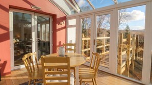 A sunlit room with a round wooden table and chairs, large glass doors leading to an outdoor deck, and a red wall. - Doire An Daimh (Acharacle)