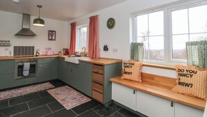 A modern kitchen with a central island, a built-in oven, and a window with curtains. - Doire An Daimh (Acharacle)