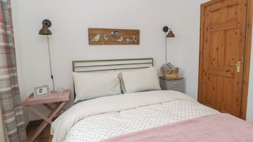 Ein Schlafzimmer mit einem Bett, einer Holztür, einem Nachttisch mit Lampe und einem an der Wand hängenden Kunstwerk.