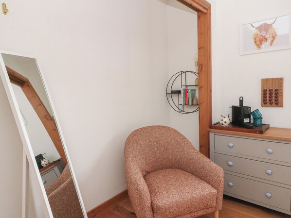 Une pièce comprenant une chaise en bois, une petite table avec une machine à café, une bibliothèque et un luminaire fixé au mur.