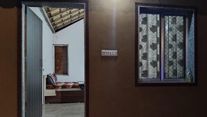 A room with a wooden door, a window with floral curtains, and a small wall-mounted light switch. - Fortune Heritage Resort  (Shri Madhopur)