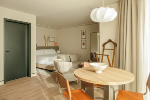 Ein modernes Hotelzimmer mit einem Bett, einer Sitzecke mit Sofa und Sesseln, einem Esstisch mit Schüssel und einem Spiegel.