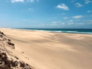 A vast sandy beach with gentle waves, clear skies, and sparse vegetation. - ROBINSON BOA VISTA - All Inclusive (Boa Vista)