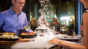 A dining table with food, a glass of wine, and a steaming dish.