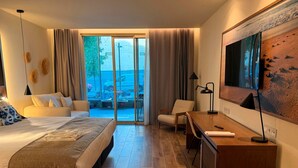 A hotel room with a bed, a desk, a chair, a TV, and a view of the outdoors.