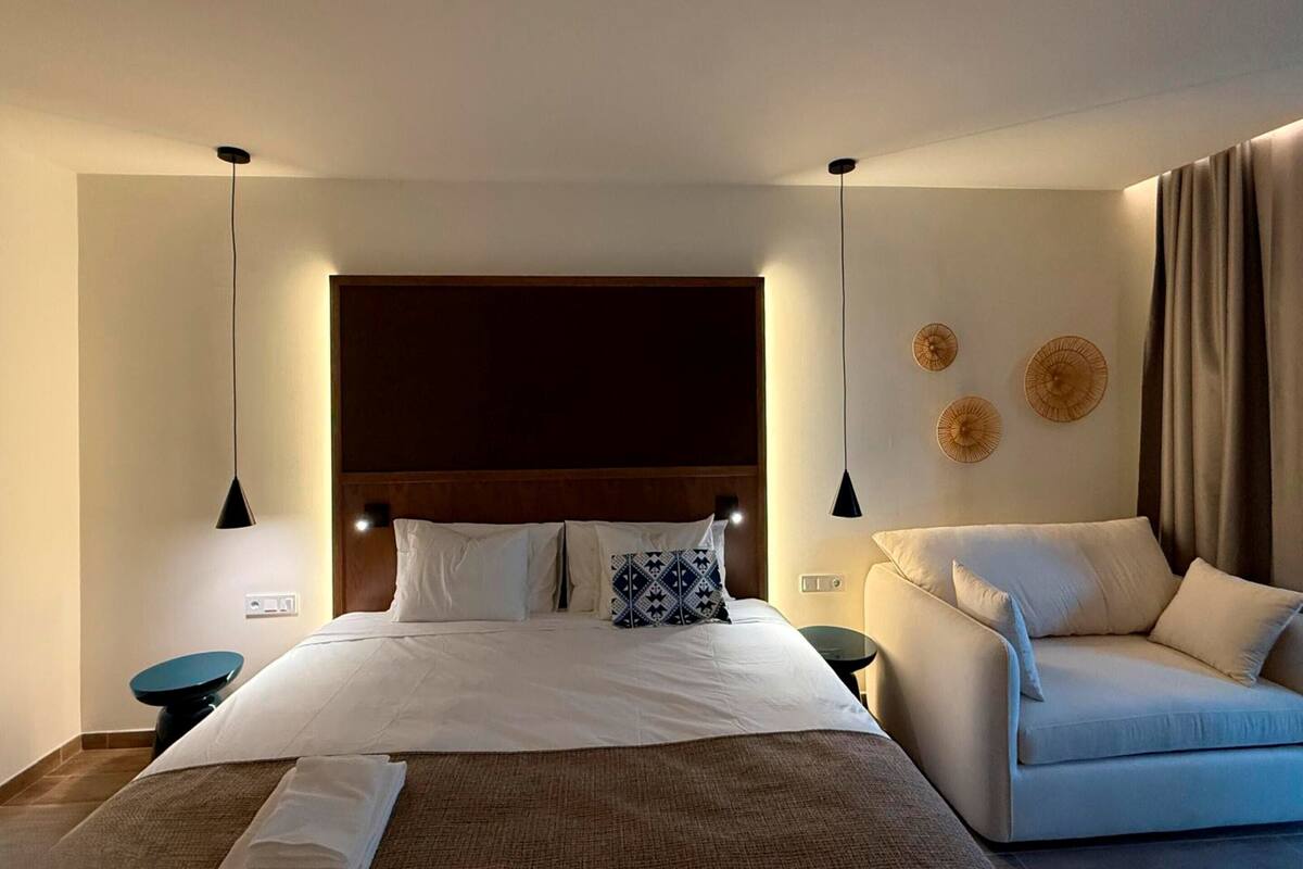 A hotel room with a large bed, two bedside tables, a sofa, and a headboard.