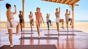 A group of people exercising on yoga mats under a wooden structure by the beach.