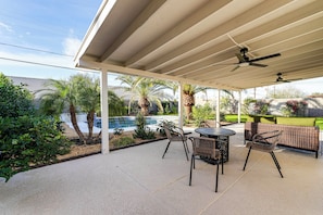 Un patio techado con piscina, mobiliario exterior y palmeras.