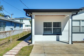 Un edificio moderno con un acceso cubierto, un camino de hormigón y una valla de malla metálica.