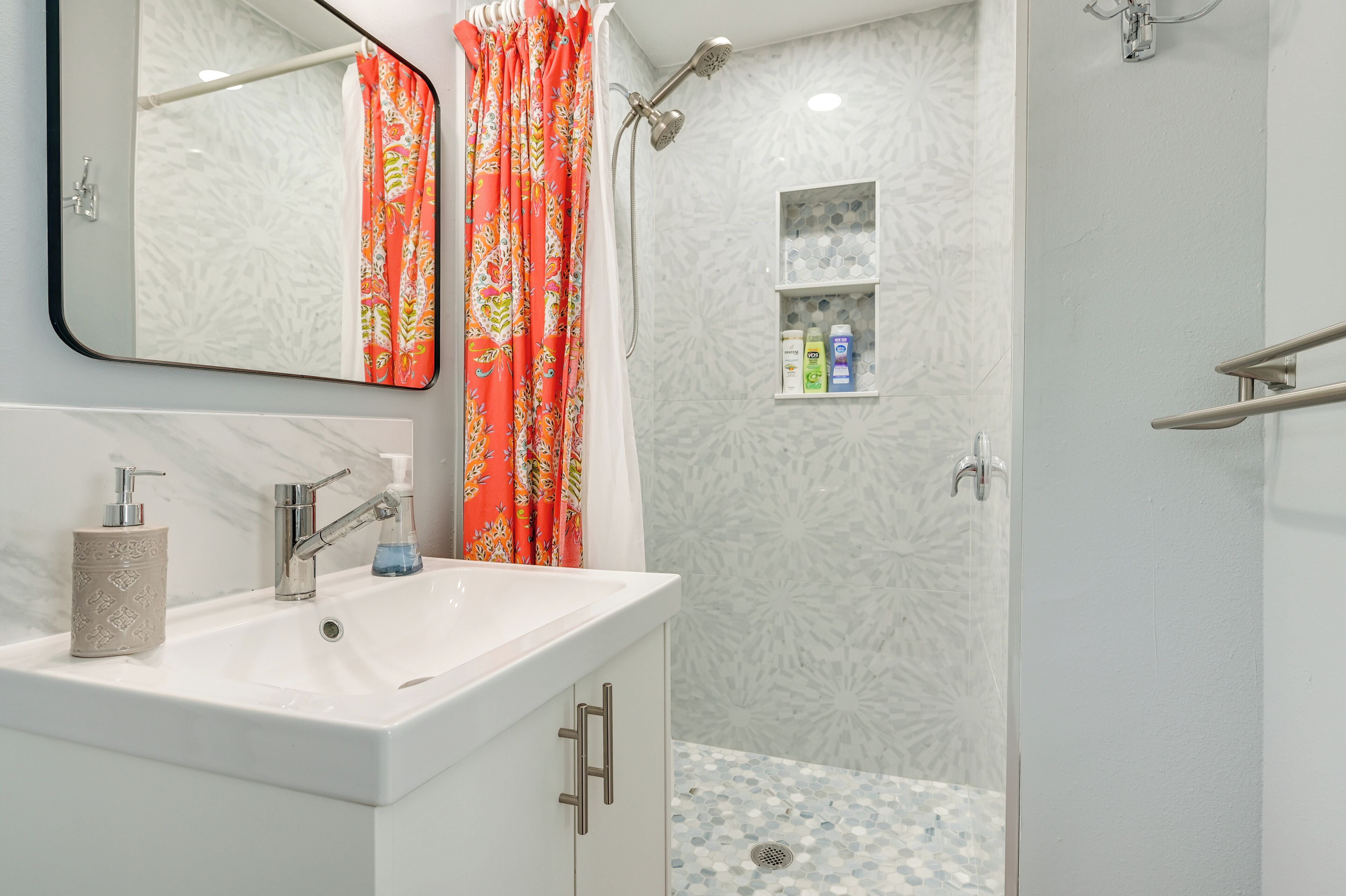 A bathroom with a white sink, a mirror, a shower with a rain showerhead, and a tiled shower floor.
