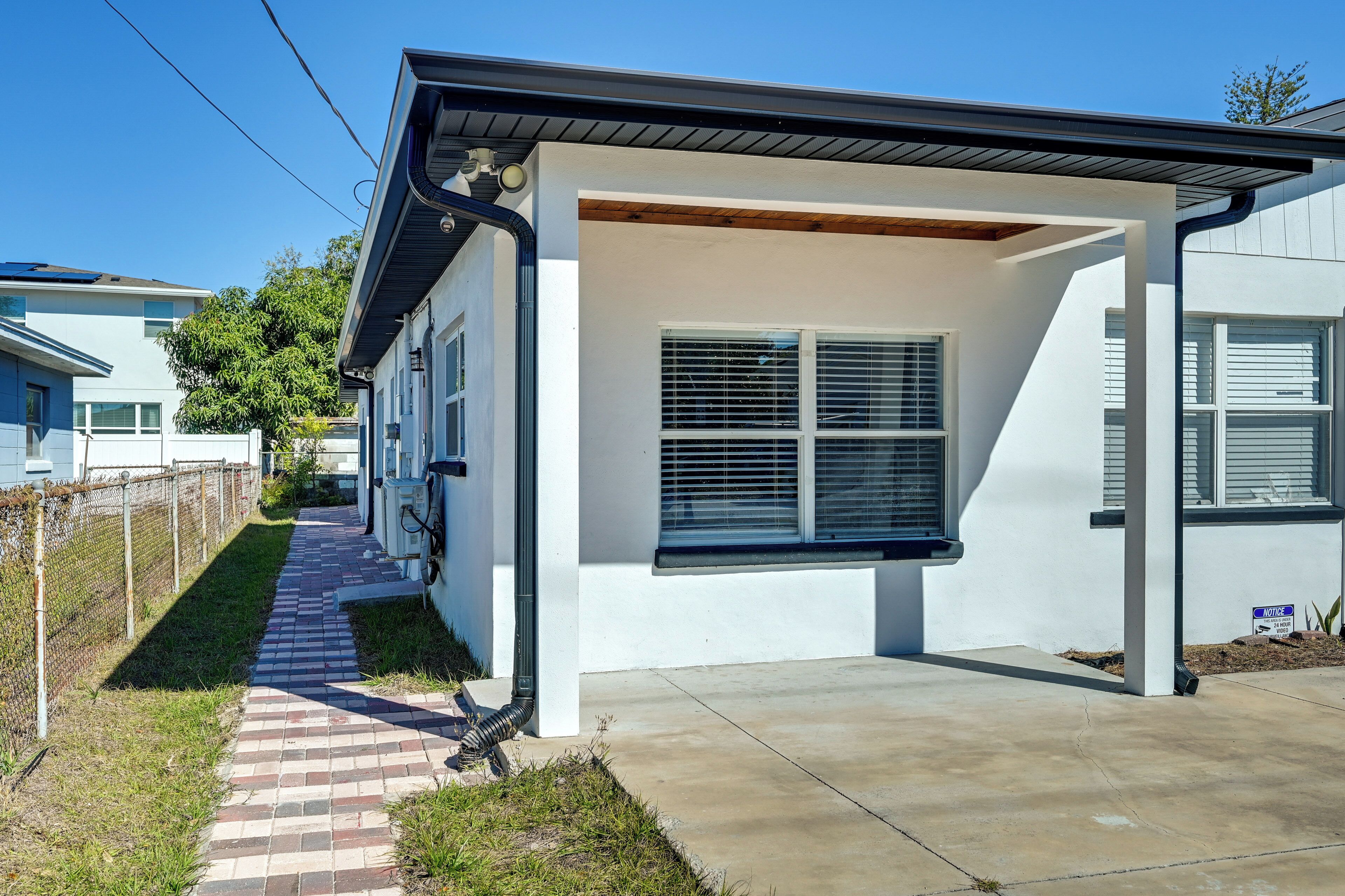 Uma casa moderna térrea com varanda coberta, um caminho de tijolos e um céu azul límpido.
