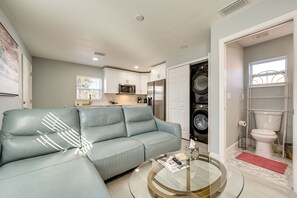Una sala moderna con un sofá de cuero azul claro, una mesa de centro de vidrio y una cocina con armarios blancos, un microondas y un refrigerador.