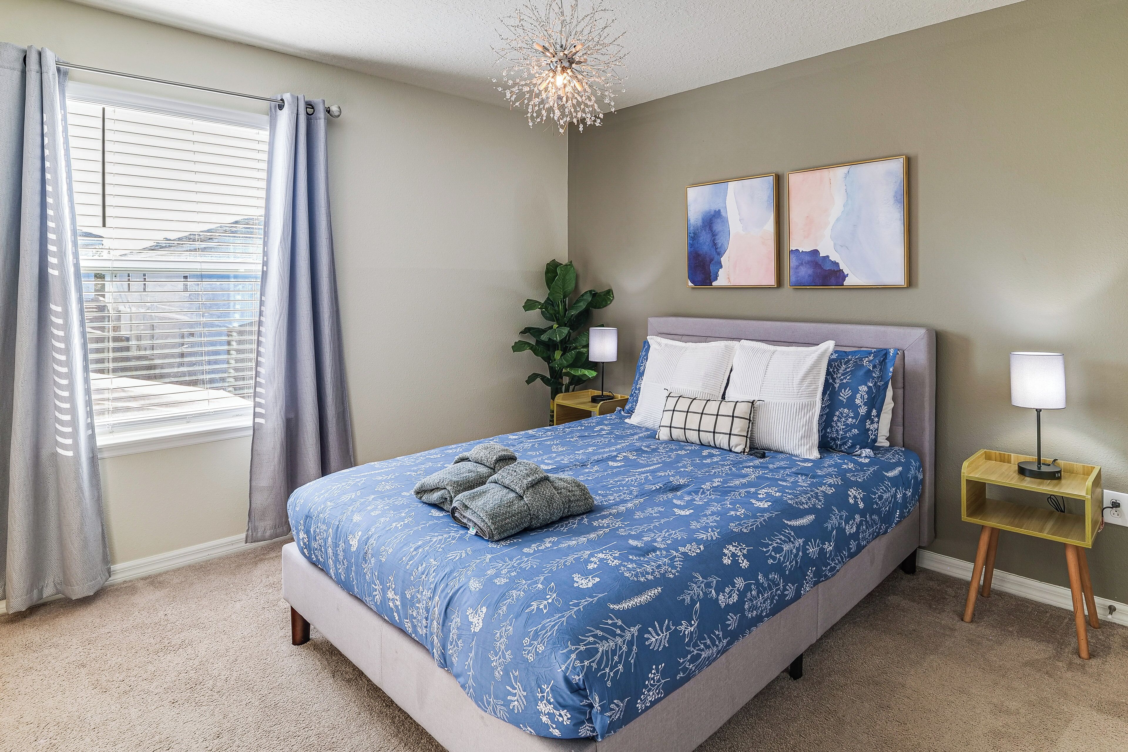 Quarto com uma cama grande, mesa de cabeceira, luminária, planta e obras de arte na parede.
