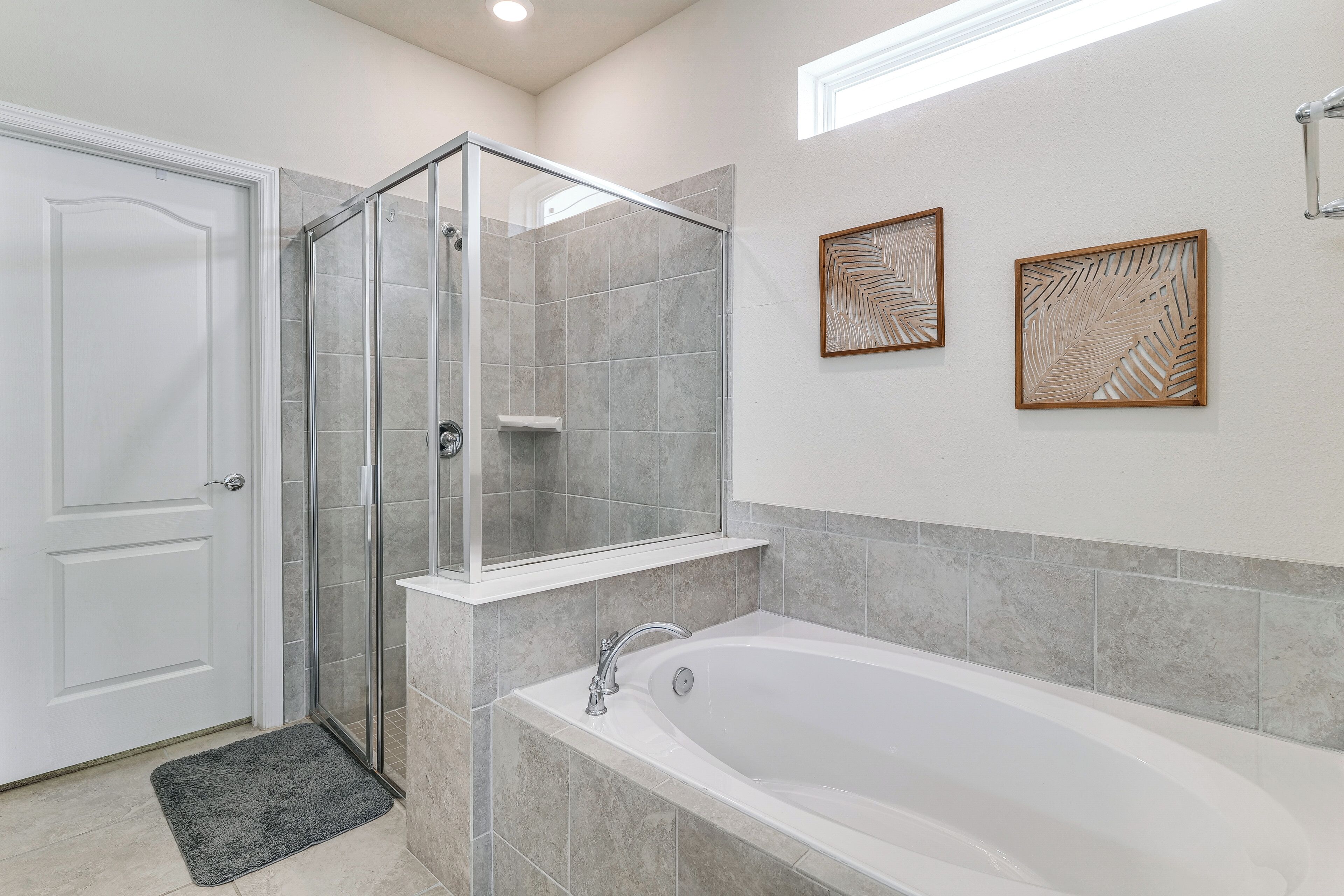 Ein Badezimmer mit einer gläsernen Duschkabine, einer Badewanne und zwei gerahmten Blattmustern an der Wand.