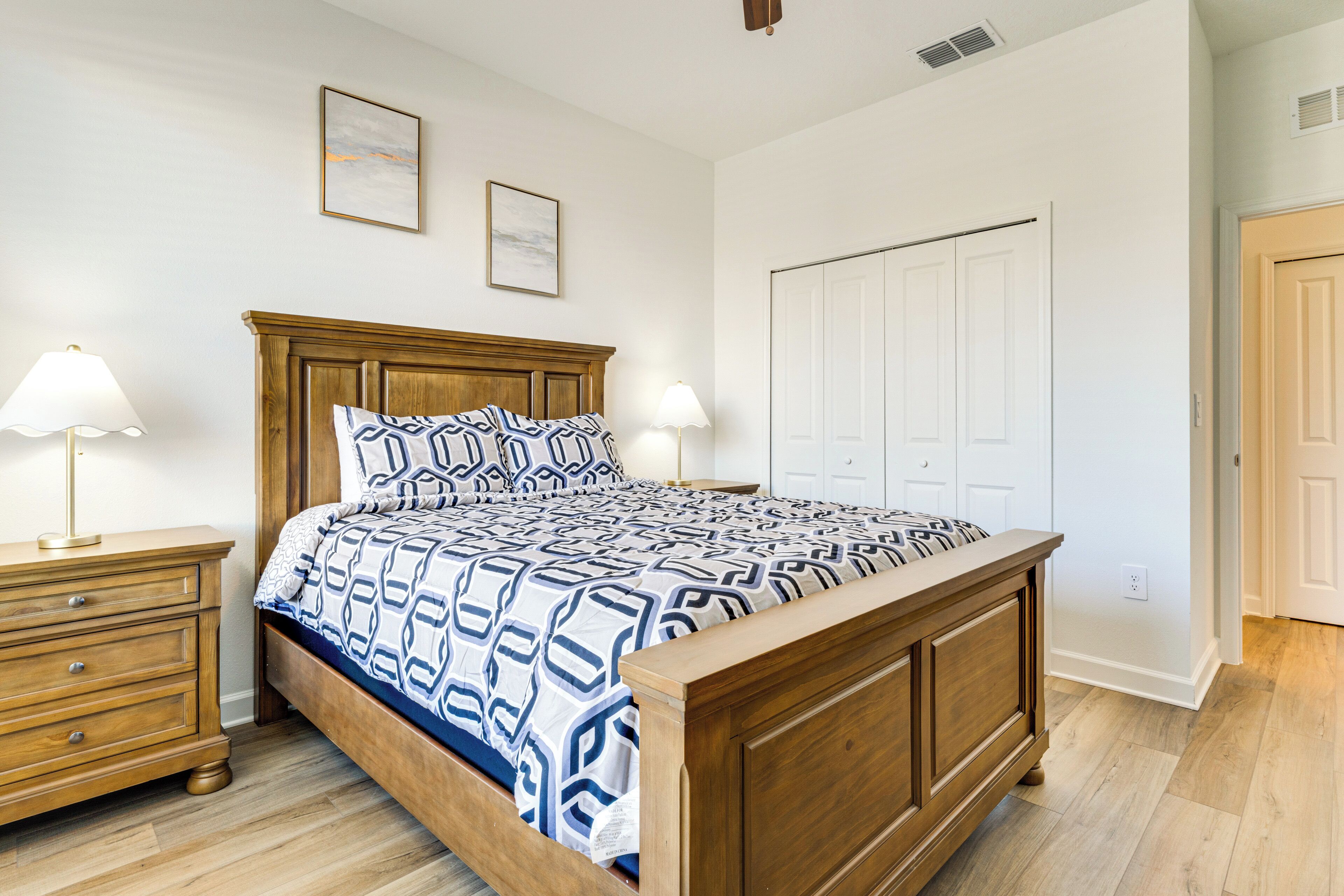 Une chambre à coucher avec un lit en bois, deux tables de chevet avec des lampes, une armoire blanche et un tableau encadré au mur.