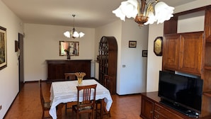 A dining area with a table set for two, a wooden cabinet with a television, and a chandelier. - La Coccinella Apartment with Better Sleep Technology (Gonars)