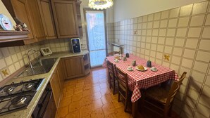 A compact kitchen with wooden cabinets, a gas stove, and a dining table set with a checkered tablecloth. - La Coccinella Apartment with Better Sleep Technology (Gonars)