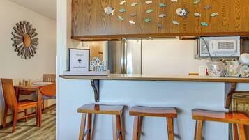 Une cuisine avec des tabourets de bar en bois, un réfrigérateur, un four à micro-ondes et un mur décoré de motifs de poissons.