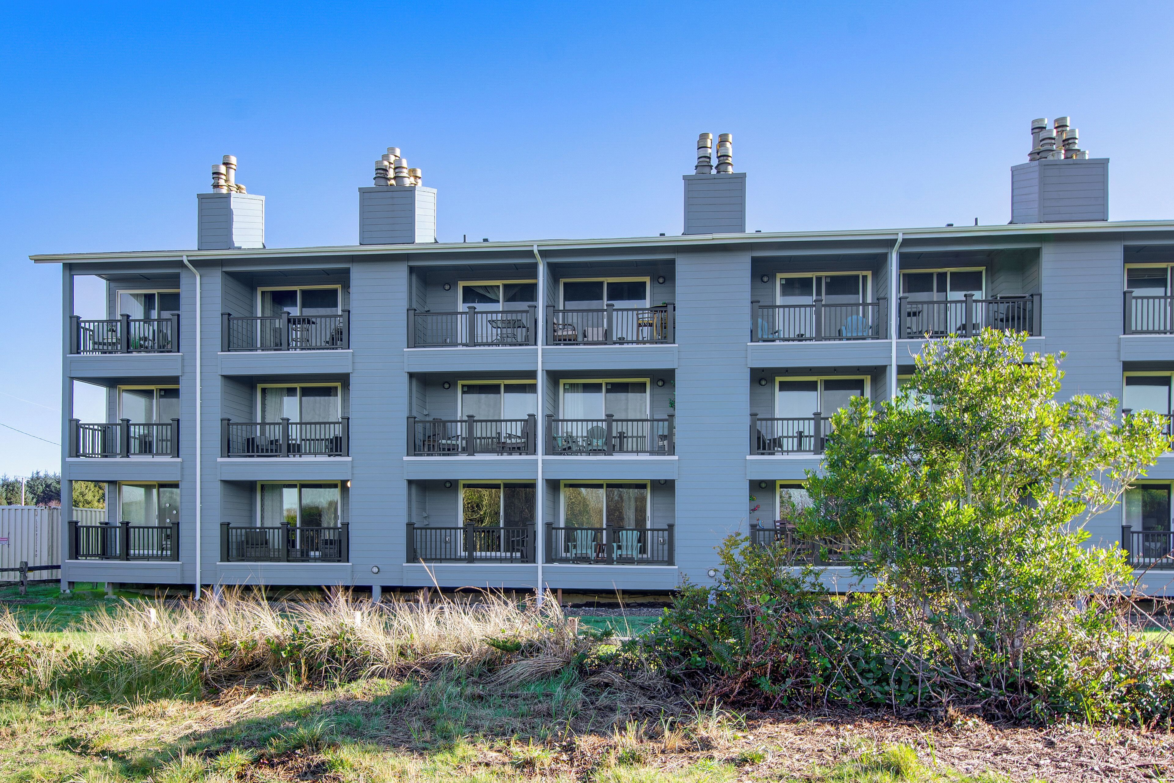 A multi-story building with balconies, a clear sky, and a tree in the foreground.