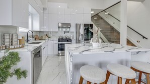 A modern kitchen with white cabinetry, a marble island, and a stainless steel range hood. - 6 Mi to Manhattan: Luxe Apt w/ City Views! (Jersey City)