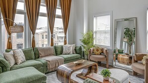 A living room with a sectional sofa, a coffee table, and a chair. There are large windows with curtains, a mirror, and a plant. - 6 Mi to Manhattan: Luxe Apt w/ City Views! (Jersey City)