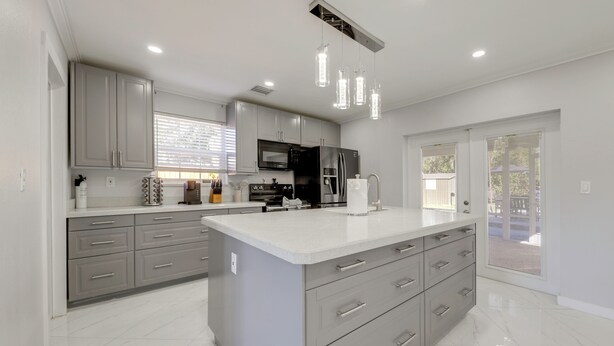 Une cuisine moderne avec des meubles gris, un grand îlot central, des appareils en acier inoxydable et des luminaires suspendus.