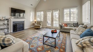 A spacious living room with a fireplace, a ceiling fan, and large windows. - 1 Mi to Bethany Beach: Family Home on Golf Course! (Bethany Beach)