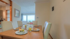 Tavola imbandita con articoli per la colazione, tra cui piatti con pasticcini, frutta e succo d'arancia, in una stanza con vista sul mare.