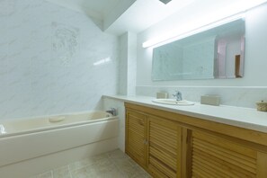 A bathroom with a bathtub, a sink, a mirror, and wooden cabinets. - Carbis Bay View (St Ives)