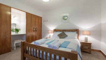 A neatly made bed with rolled towels, a bedside table with a lamp, a wooden wardrobe, and a small bench.