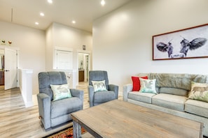 Una sala de estar con dos sillones grises, una mesa de centro de madera y un sofá gris con cojines rojos y verdes.