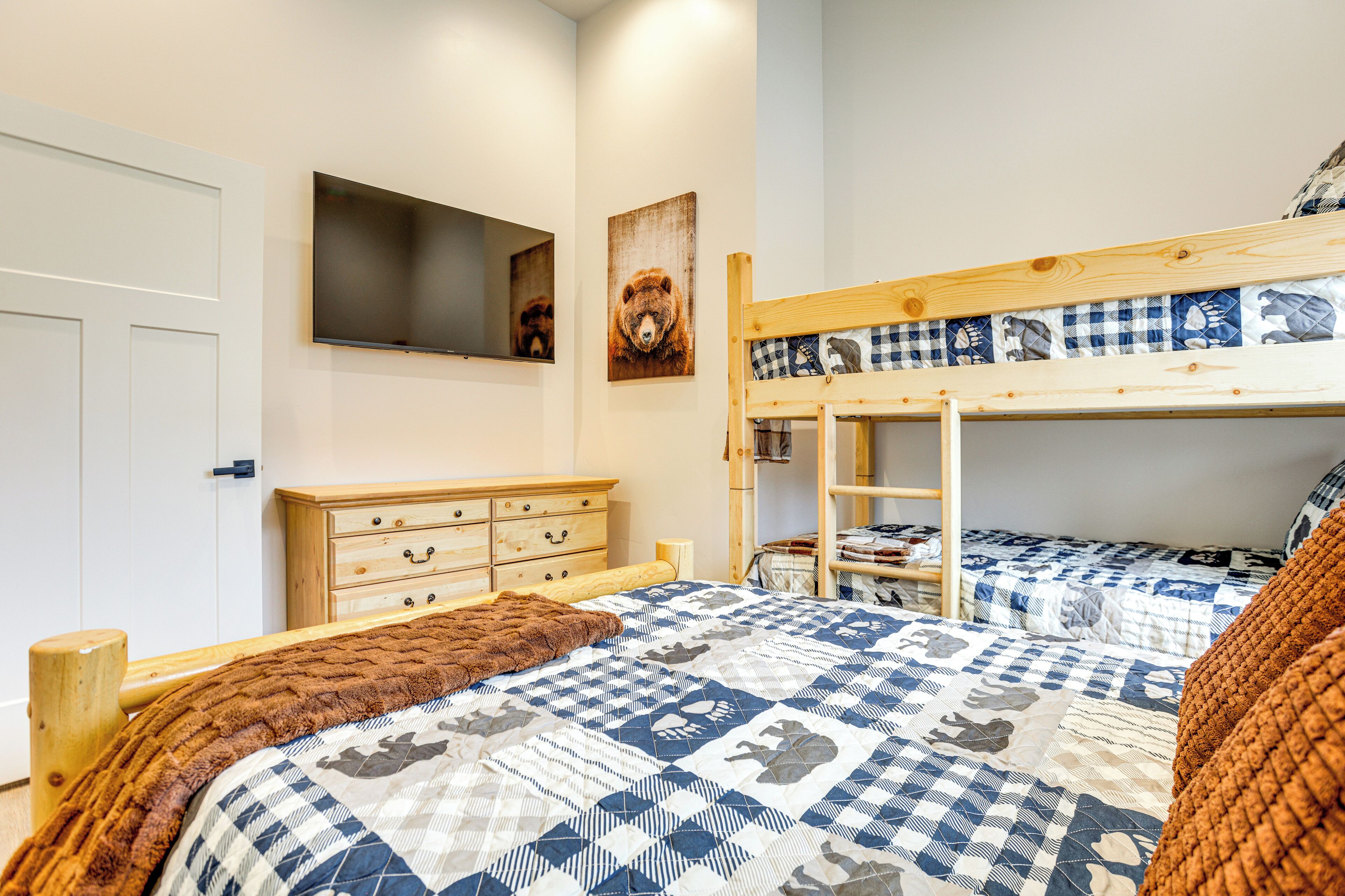 Un dormitorio con una litera, un aparador de madera, un televisor montado en la pared y una decoración de pared con temática de osos.