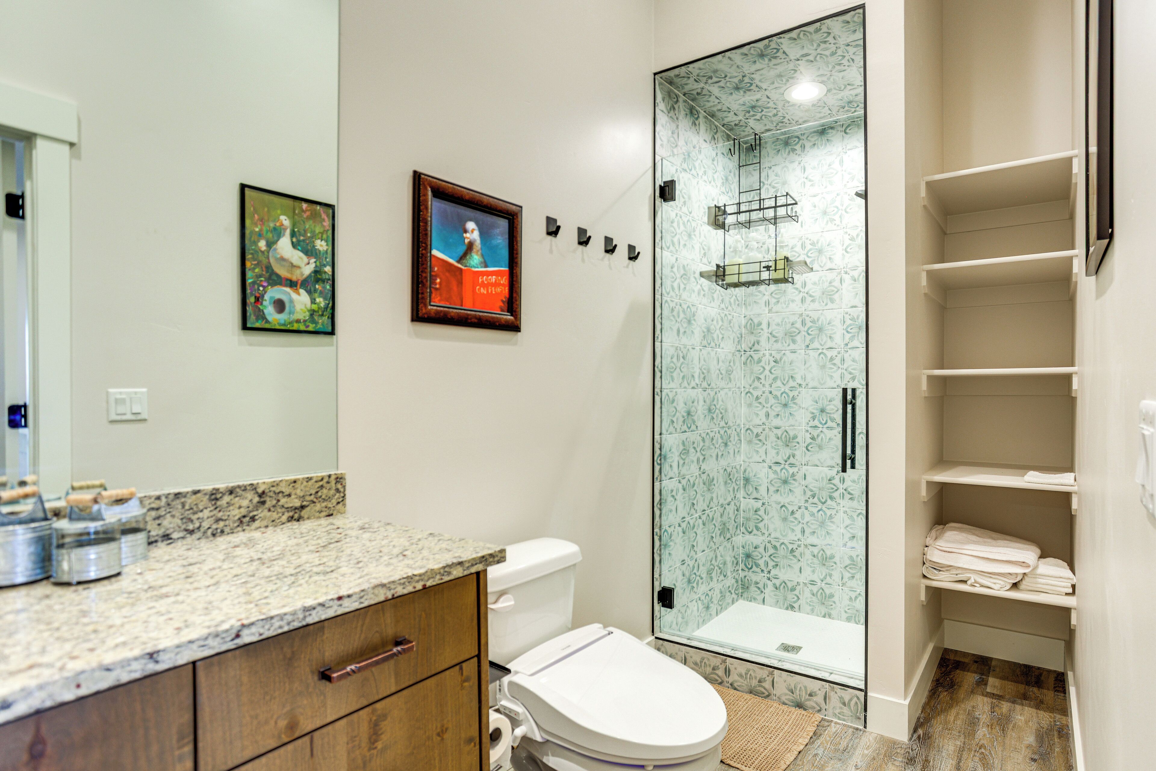 A bathroom with a granite countertop, a toilet, a glass shower enclosure, and a towel rack.