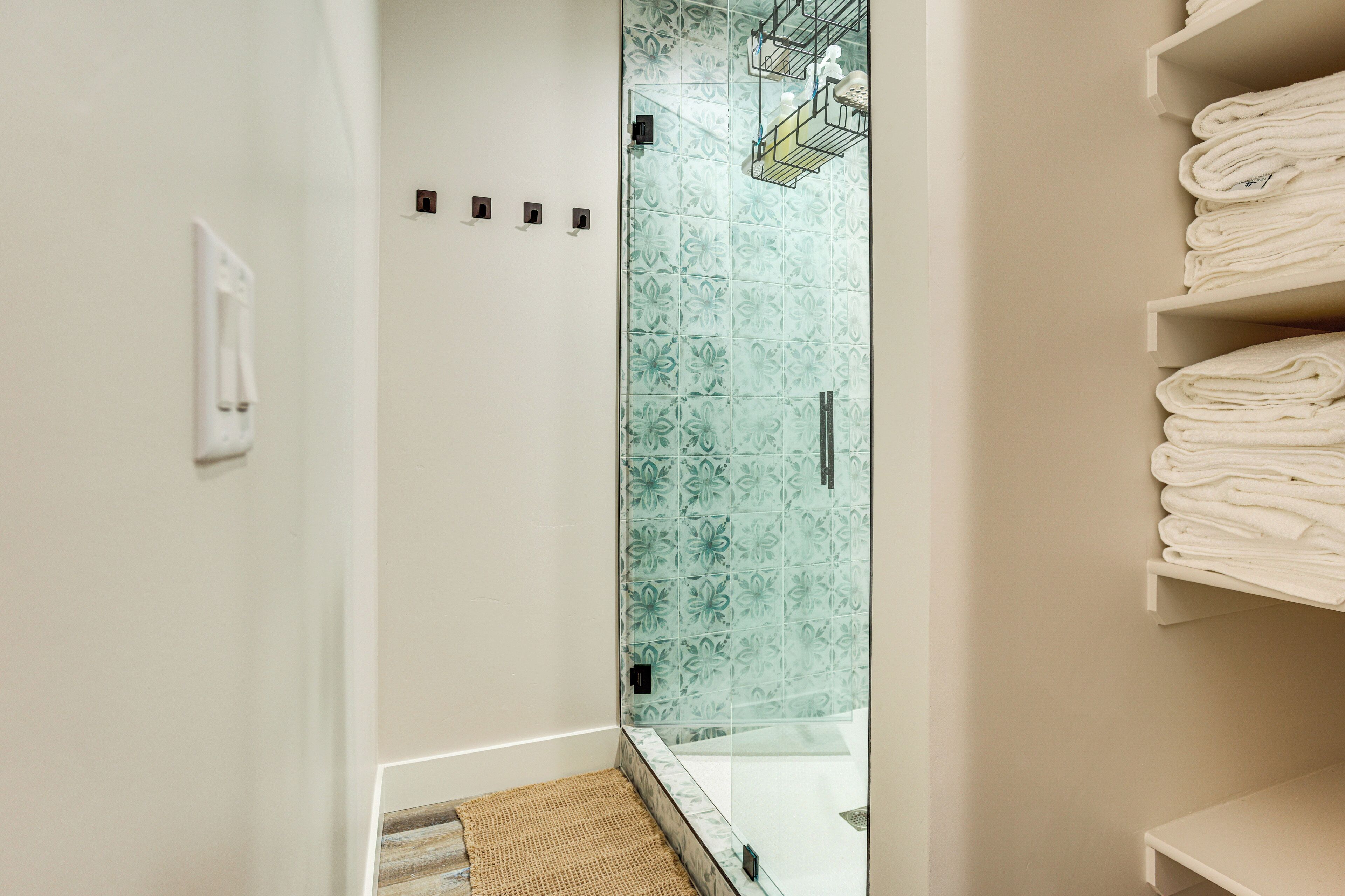 A bathroom with a glass shower enclosure, a towel rack, and a small rug.