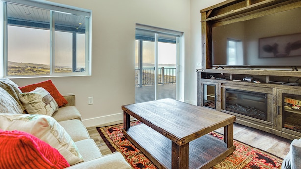 A living room with a sofa, a coffee table, a fireplace, and a large TV. - Hot Tub & Pickleball Court: Huge Bear Lake Home! (Garden City)