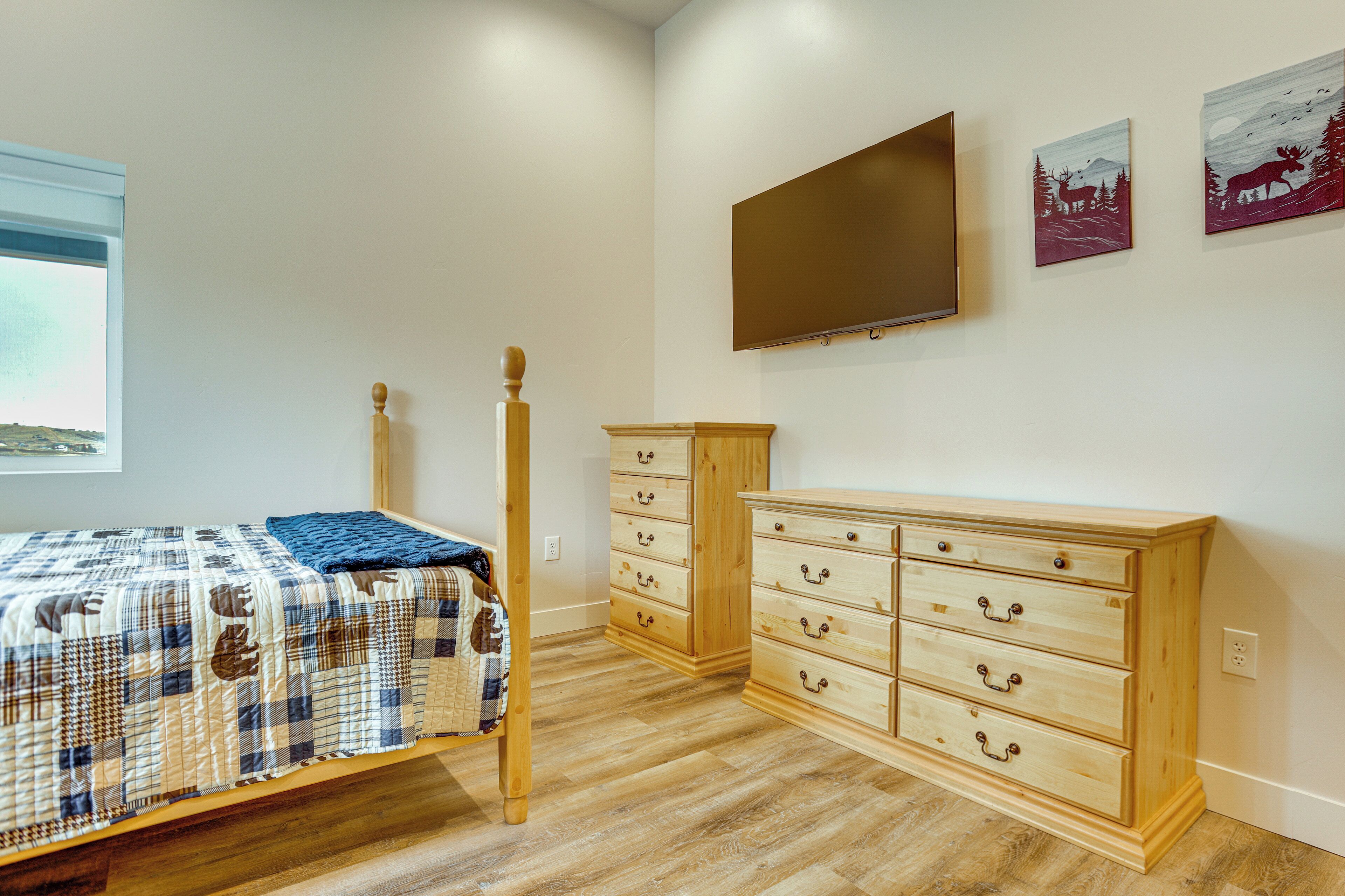 Un dormitorio con cama, cómoda de madera y televisor montado en la pared.