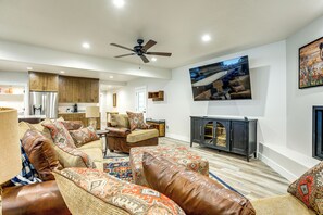 Una sala de estar amplia con un sofá de cuero marrón grande, una mesa de centro de madera y un televisor montado en la pared.