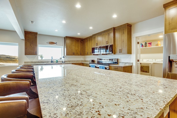 Una cocina con encimeras de granito, armarios de madera, electrodomésticos de acero inoxidable y una isla grande con taburetes de bar.