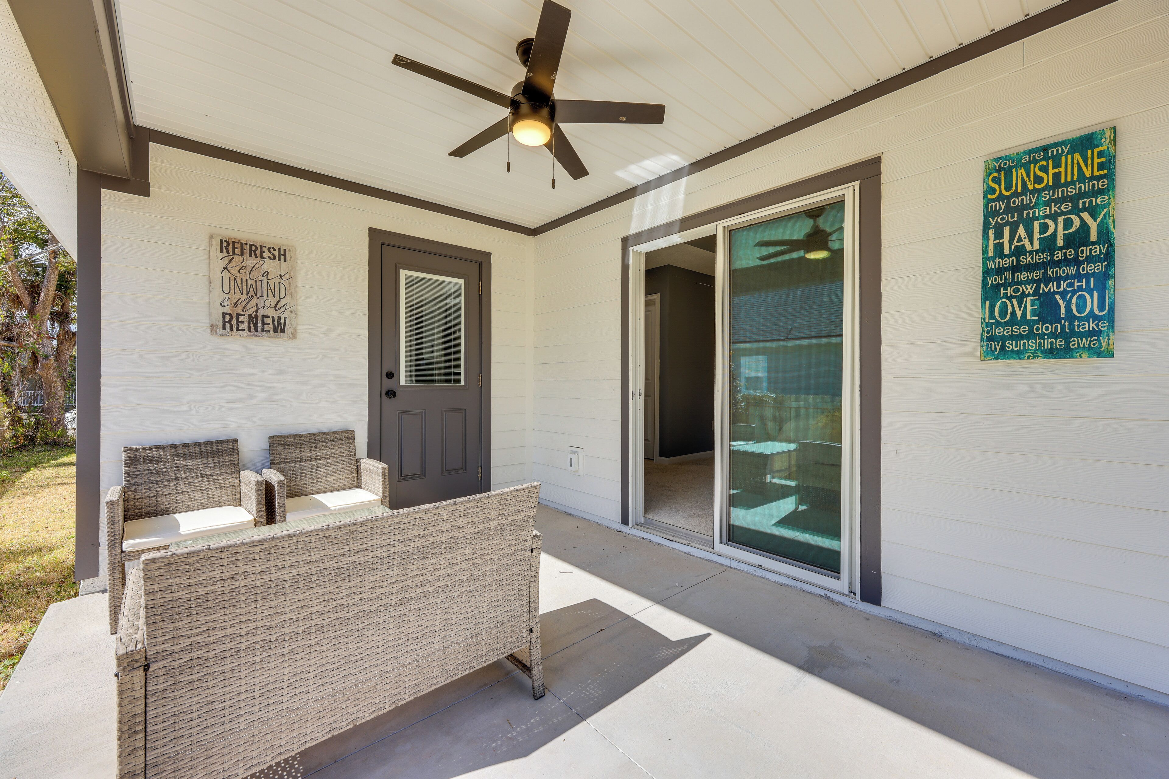 A covered porch with a ceiling fan, wicker furniture, and a sliding glass door.