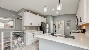 Een moderne keuken met witte kasten, een groot eiland, barkrukken en hanglampen.