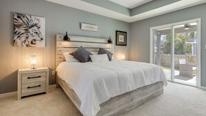 Een slaapkamer met een bed, nachtkastjes, een wandlamp, een ingelijst schilderij en een schuifdeur naar buiten.