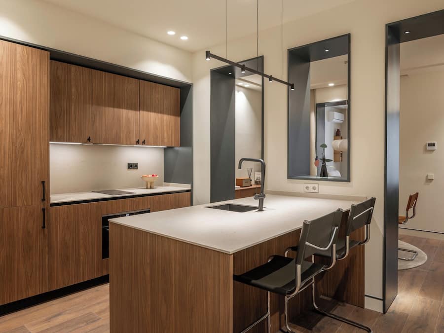 A modern kitchen with wooden cabinets, a central island with chairs, and a large mirror.