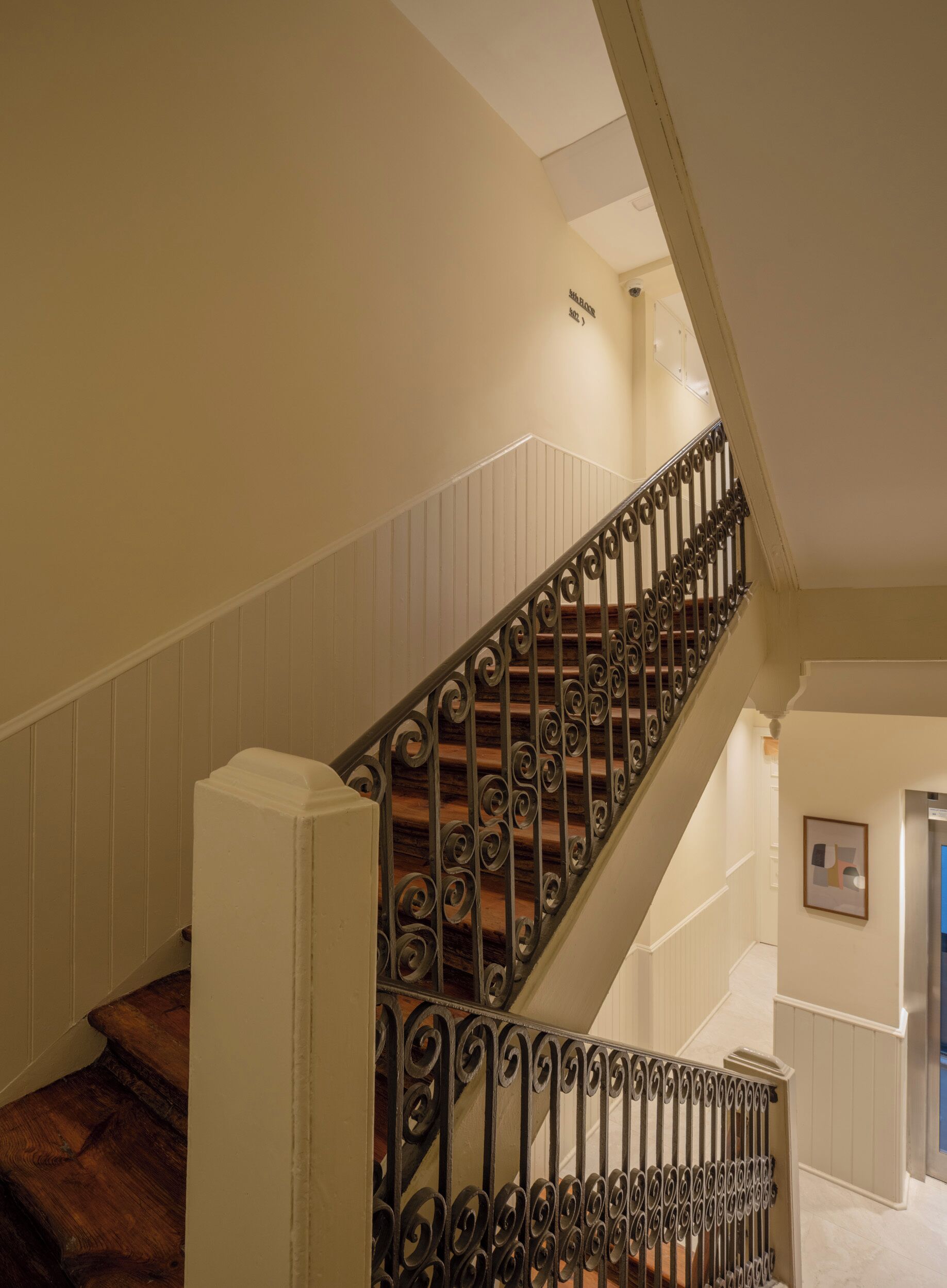 Una escalera con barandilla de madera y balaustres de metal decorativos.