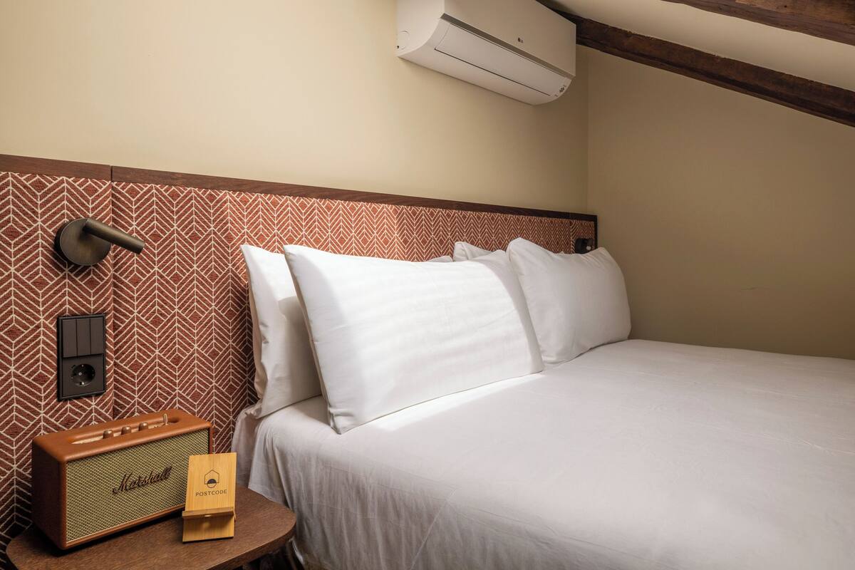 Une chambre d’hôtel avec un lit, un climatiseur fixé au mur, un papier peint à motifs et une radio de style rétro.
