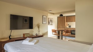A hotel room with a bed, a desk, a chair, a television, and a kitchenette. - POSTCODE Chueca (Madrid)
